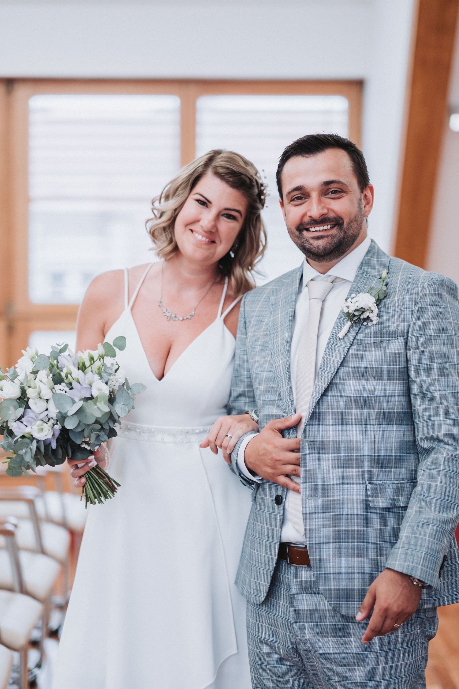 Newlywed couple in white dress and gray plaid suit smiling together during their wedding ceremony.