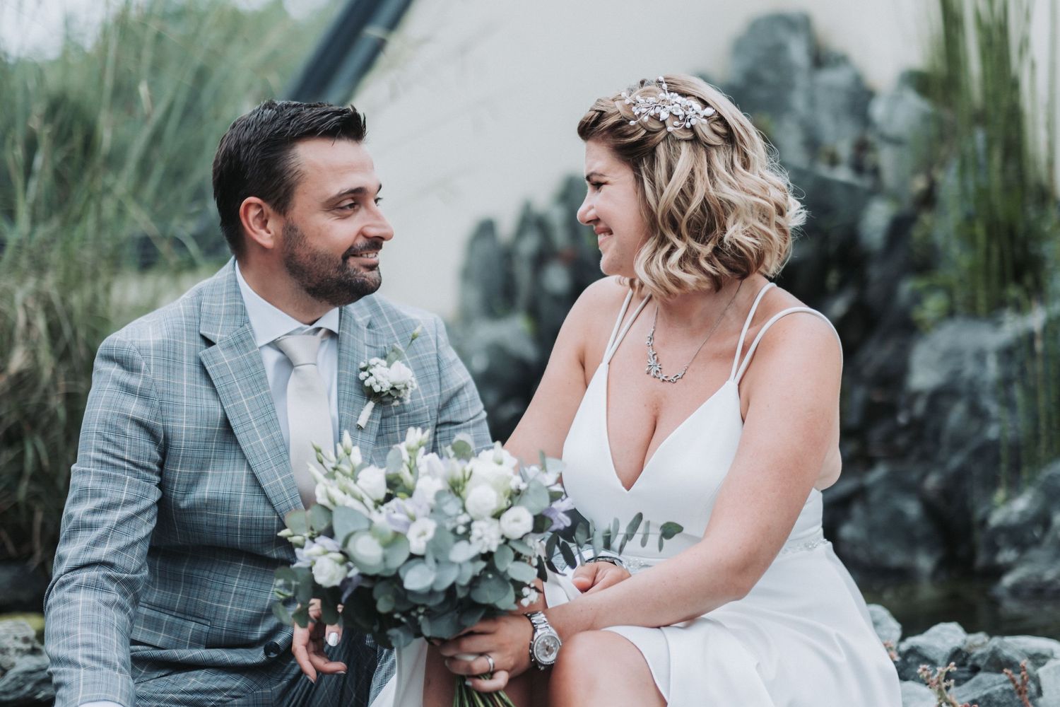 Wedding couple sharing intimate moment while seated outdoors with eucalyptus bouquet.
