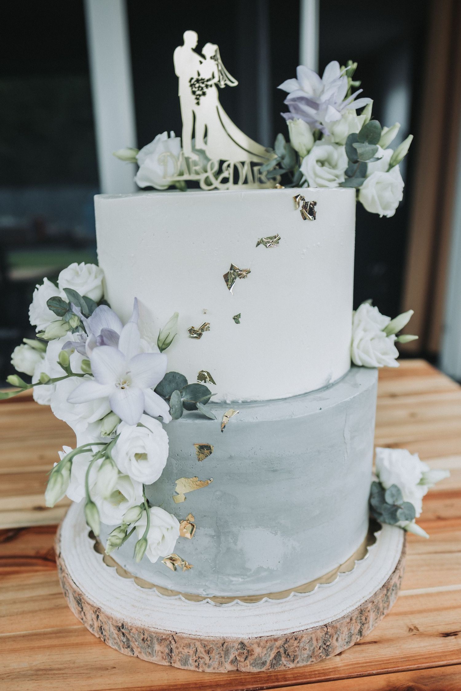 Two-tier white and gray wedding cake decorated with delicate flowers and a silhouette cake topper.