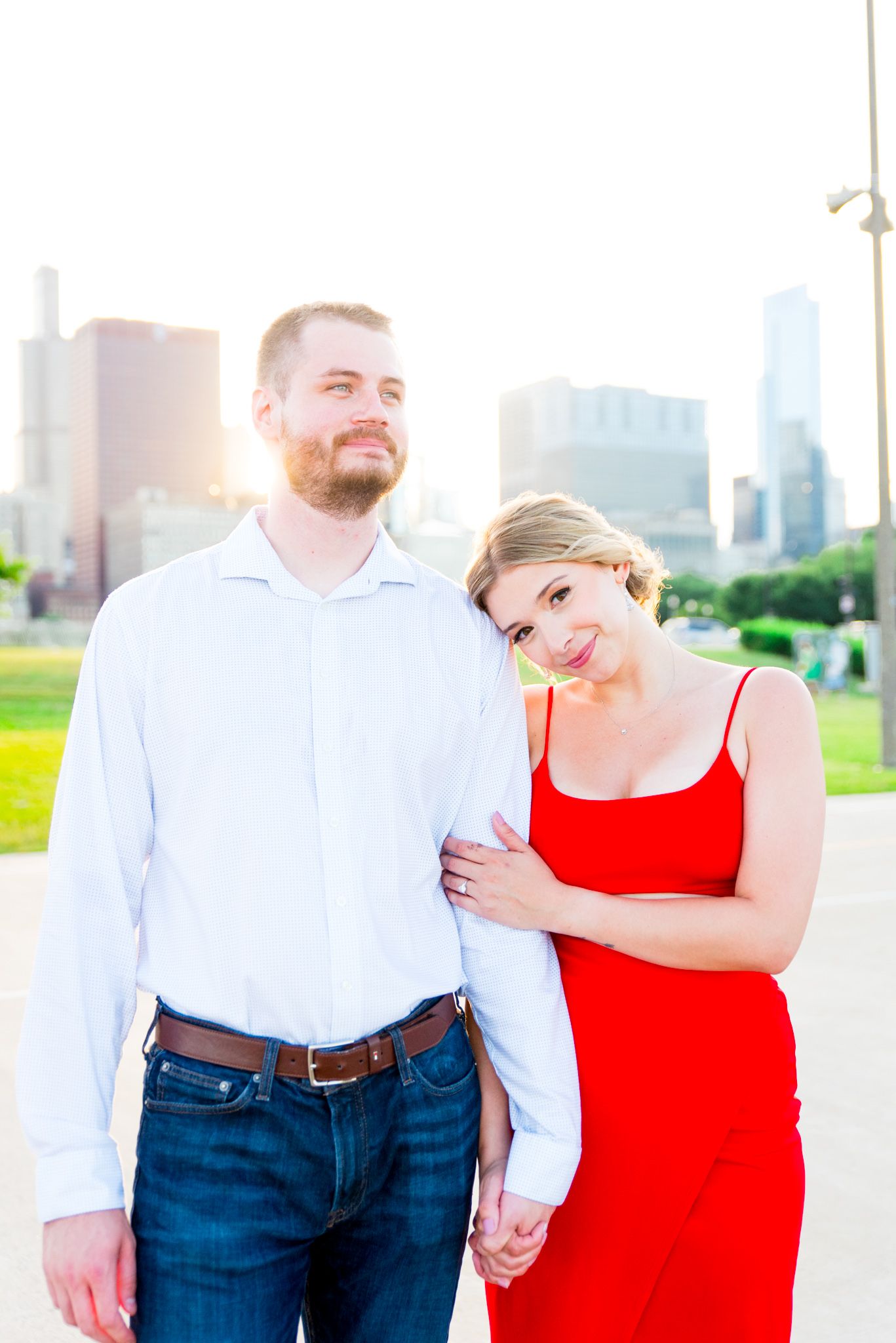 blonde woman in red dress leaning on fiance in white shirt at sunset next to Chicago lakefront trail
