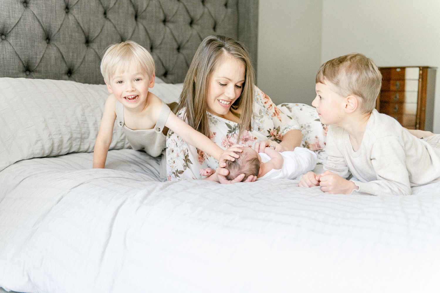 Big brother smiles as he pats his newborn sister's head as his mother smiles down at her