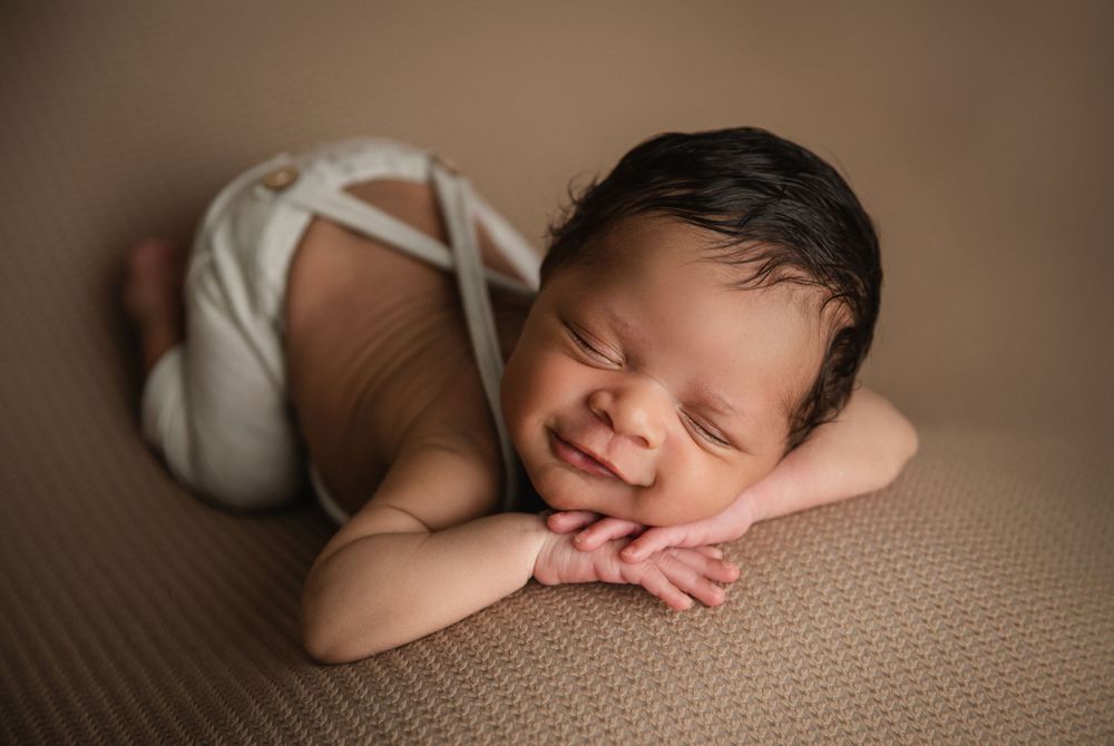 Peaceful sleeping newborn posed on brown backdrop in simple white wrap.