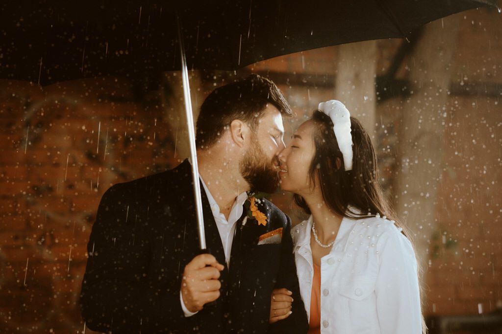 A romantic couple sharing a moment in the rain while holding an umbrella.
