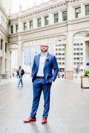 man in navy suit and glasses standing under Wrigley Building Chicago