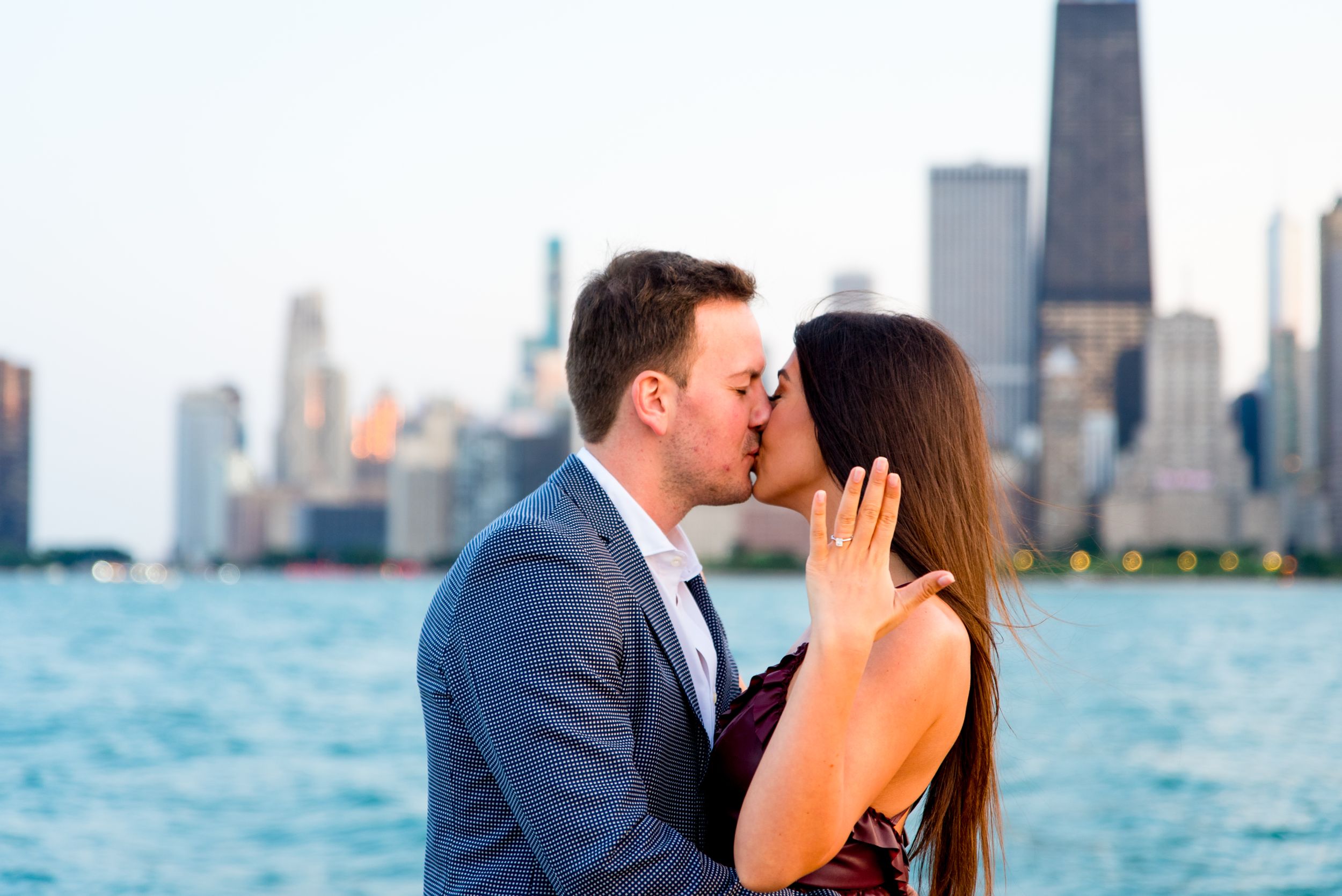 man and woman kissing and woman holding up hand in front of skyline after Chicago Proposal