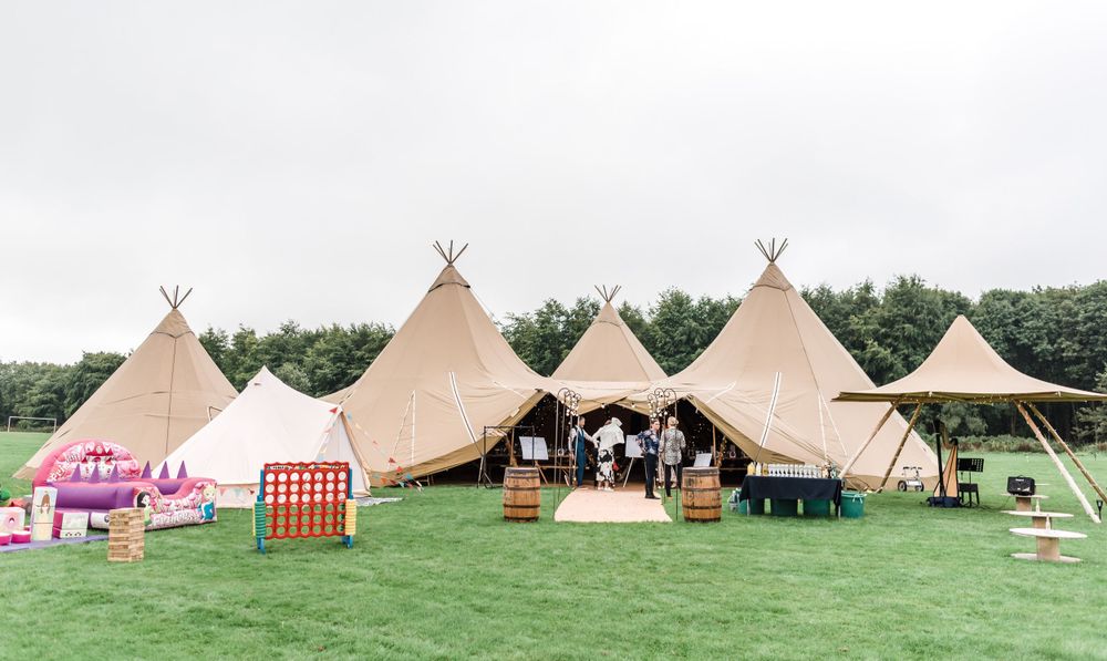 Row of five tipi tents set up on green field for outdoor wedding celebration.