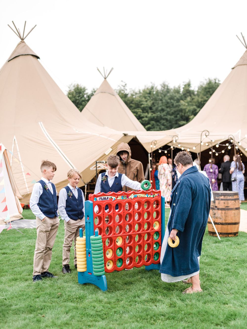 Wedding guests playing giant Connect Four game near teepee tents during outdoor reception.