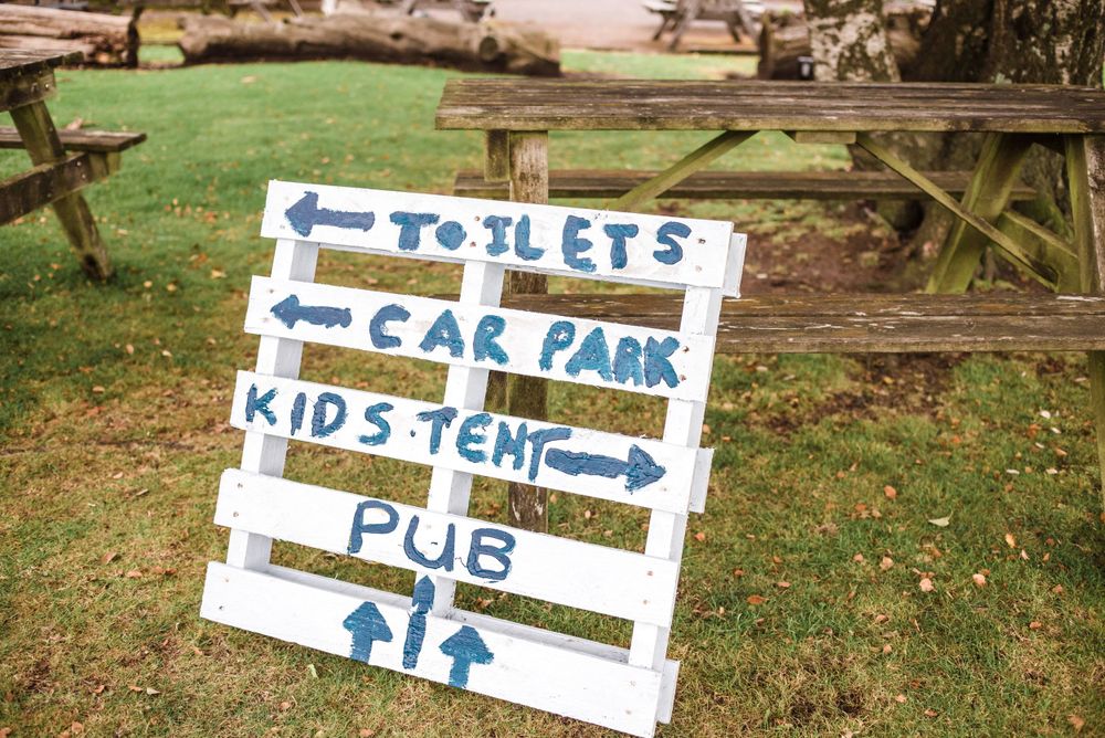 Directional wedding sign pointing to toilets, car park, kids tent, and pub areas.