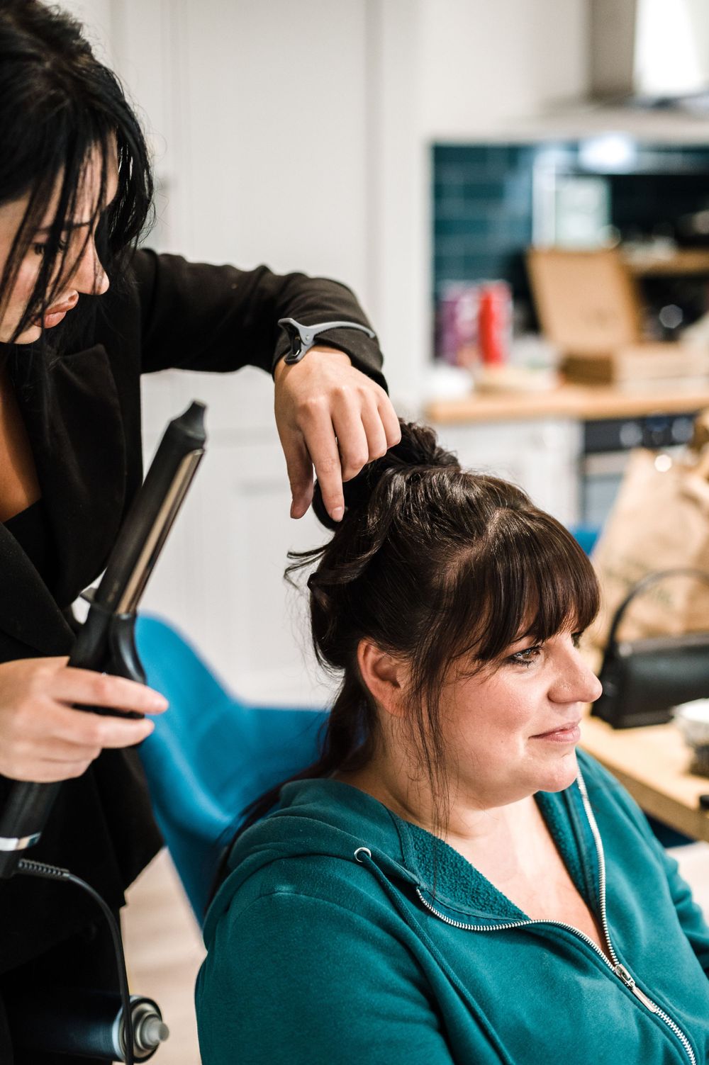 Hair styling session in progress with a teal chair and styling tools.