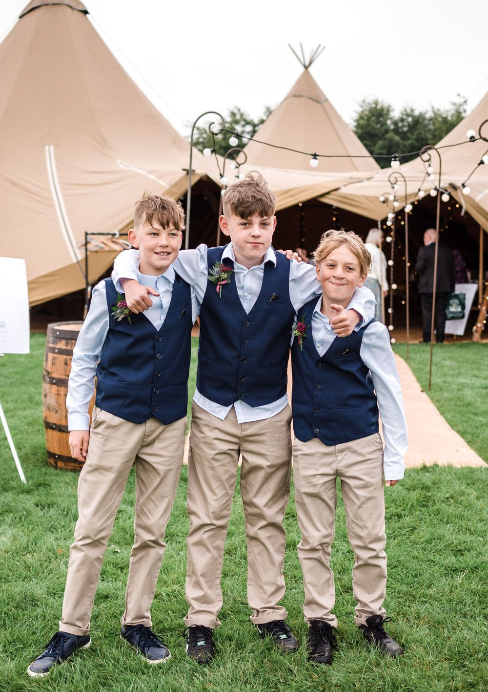 Young attendees in matching navy vests and khaki pants pose in front of teepee tent.