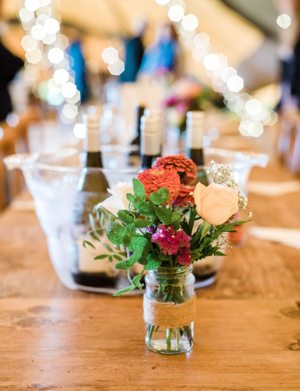 Rustic wedding table centerpiece with fresh flowers in mason jar and sparkling wine glasses.