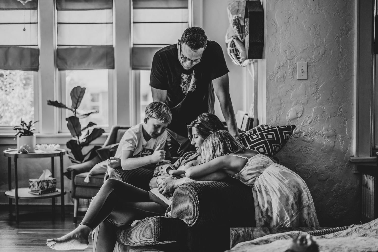 family of five in living room. all crowded around mom and new baby, seated on chair.