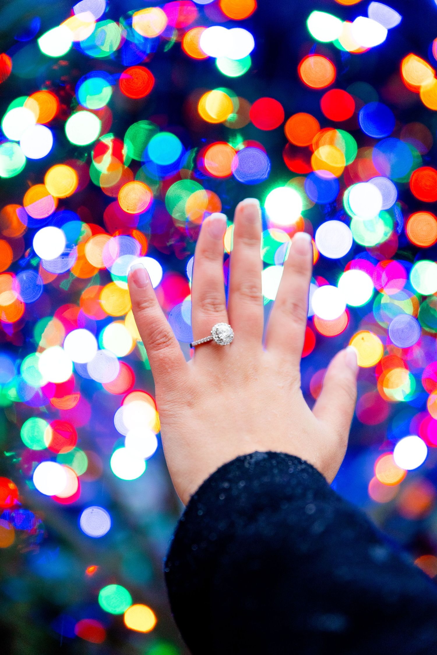 holding hand up with engagement ring in front of Millennium Park Christmas Tree