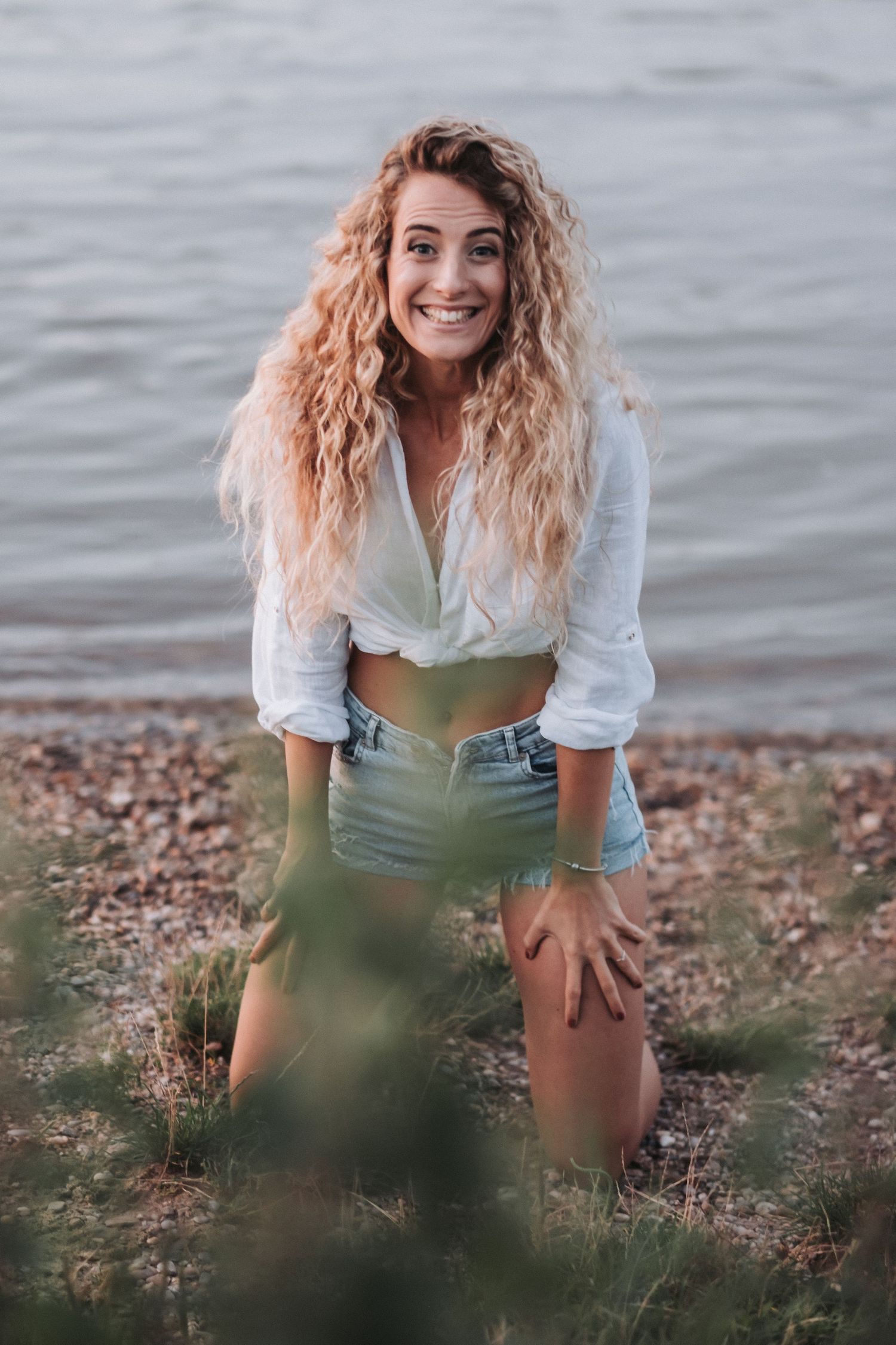 Candid laughing portrait in white crop top and shorts by the water.