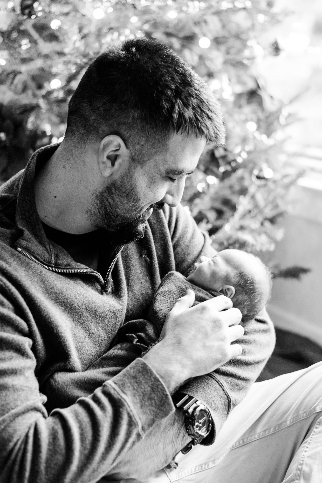 Lifestyle father holding newborn baby in pink wrap in front of Christmas tree in Pittsburgh, Pennsylvania
