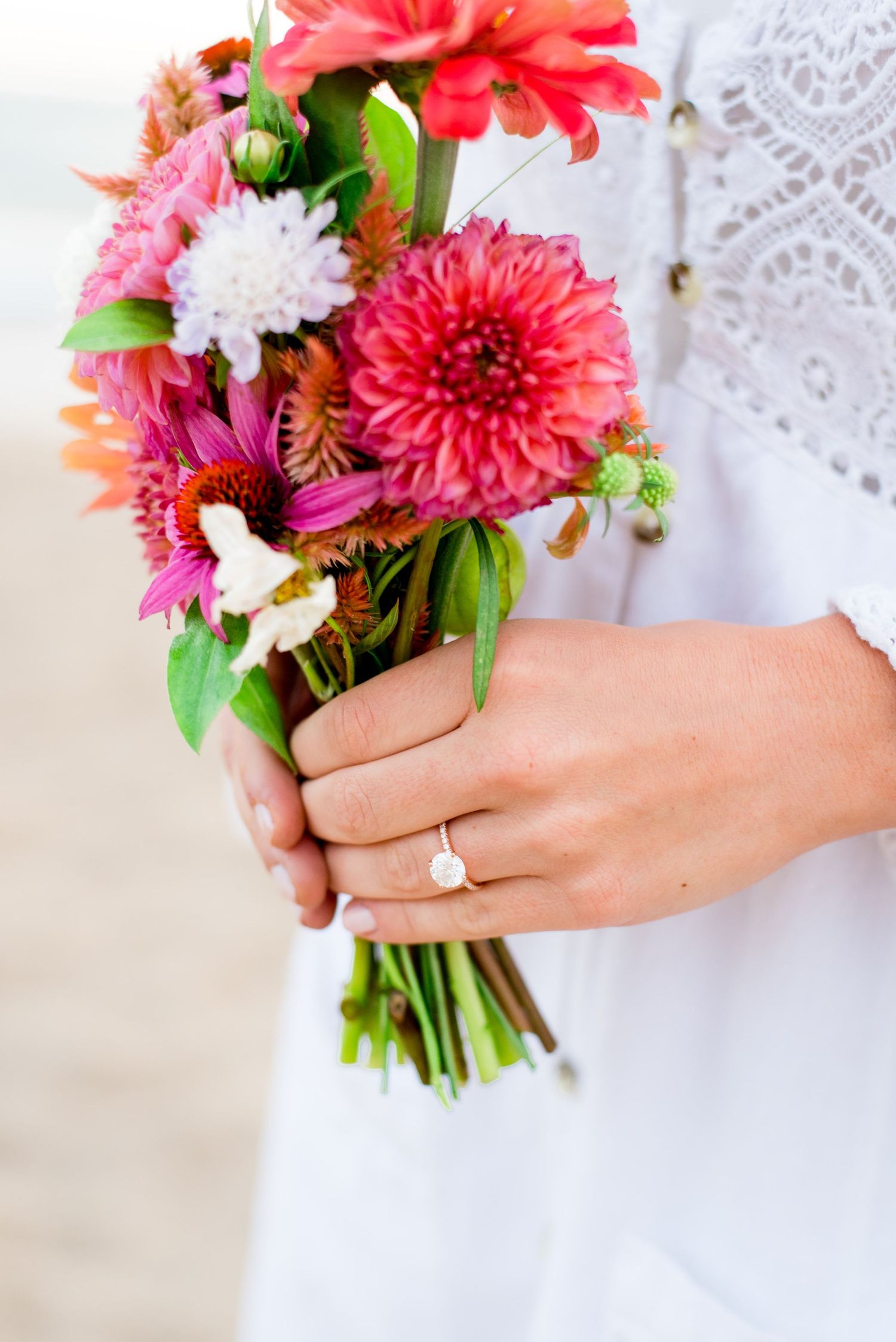 hands with engagement ring holding a pink and orange bouquet of flowers