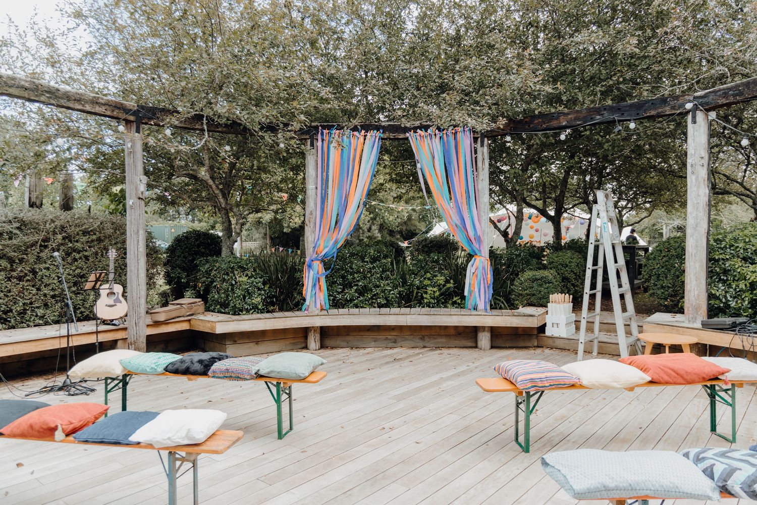 Outdoor seating area with wooden benches and colorful curtains hanging from pergola.