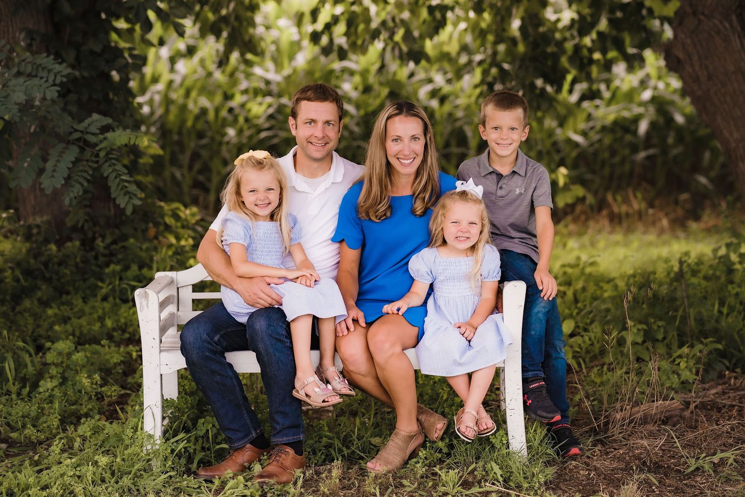 Family sitting together on a white bench in a lush garden setting.