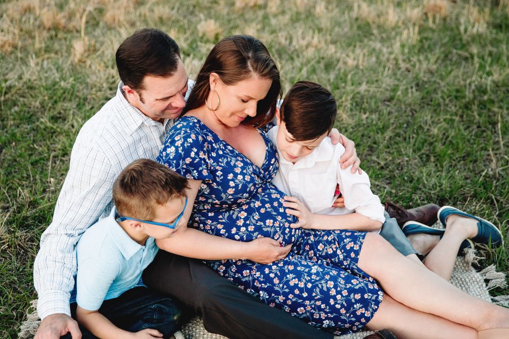 family of 4 sits on blanket in grass field