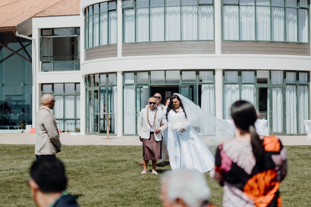 Wedding celebration outside a modern architectural building with curved glass windows.
