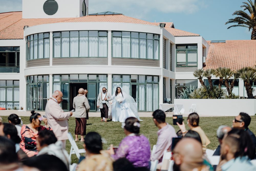 Wedding ceremony in progress outside a curved modern building with palm trees.