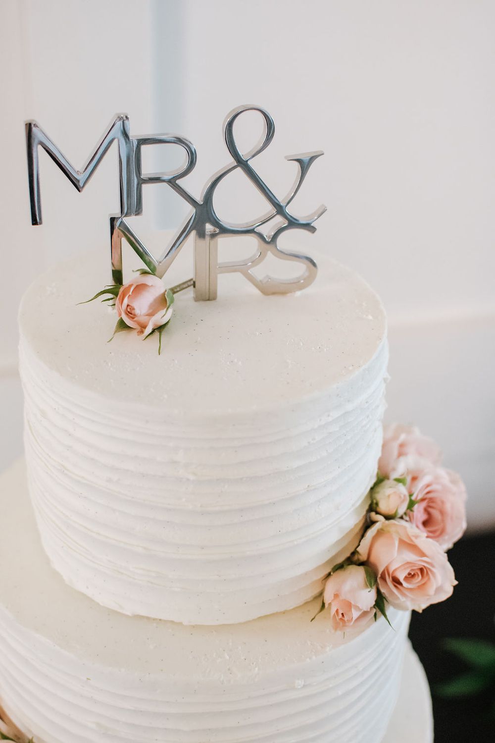 White wedding cake decorated with Mr & Mrs metallic topper and pink roses.