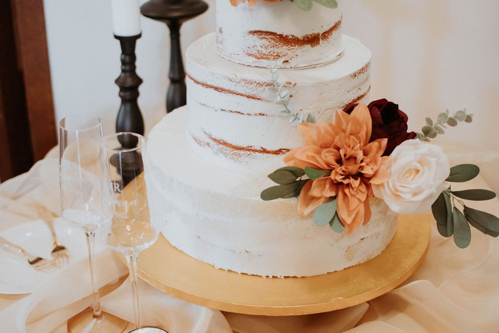 Close-up of rustic white wedding cake with orange floral decorations and eucalyptus leaves.