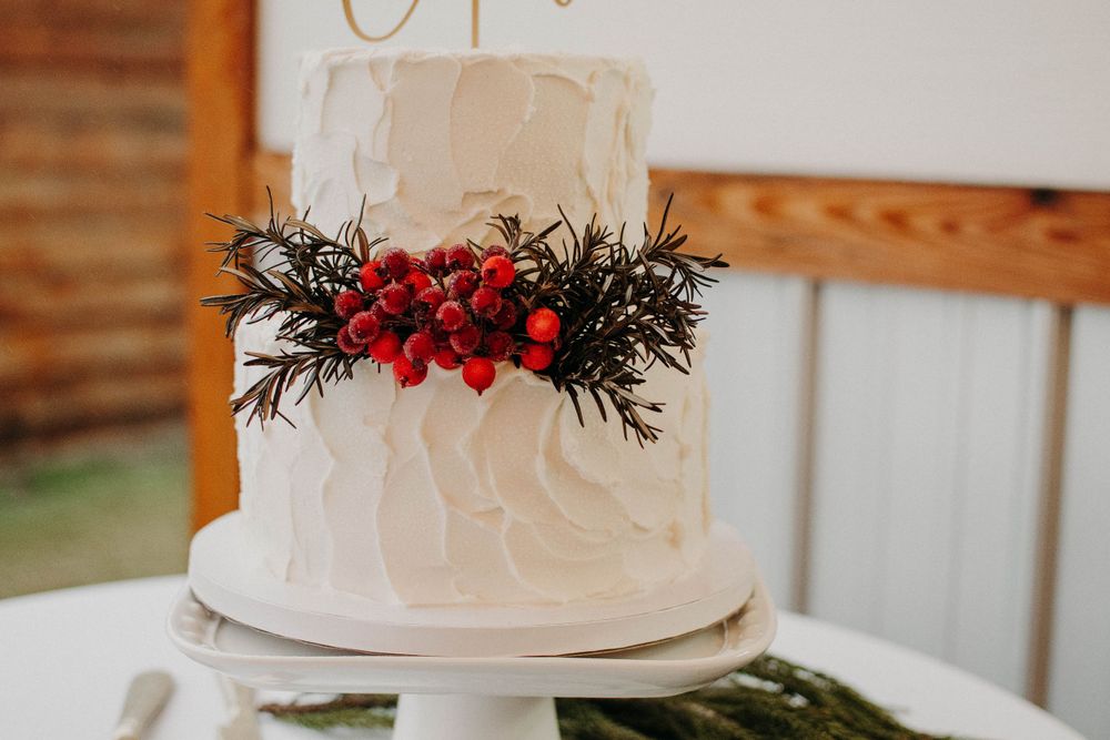 White textured wedding cake decorated with red berries and pine branches.