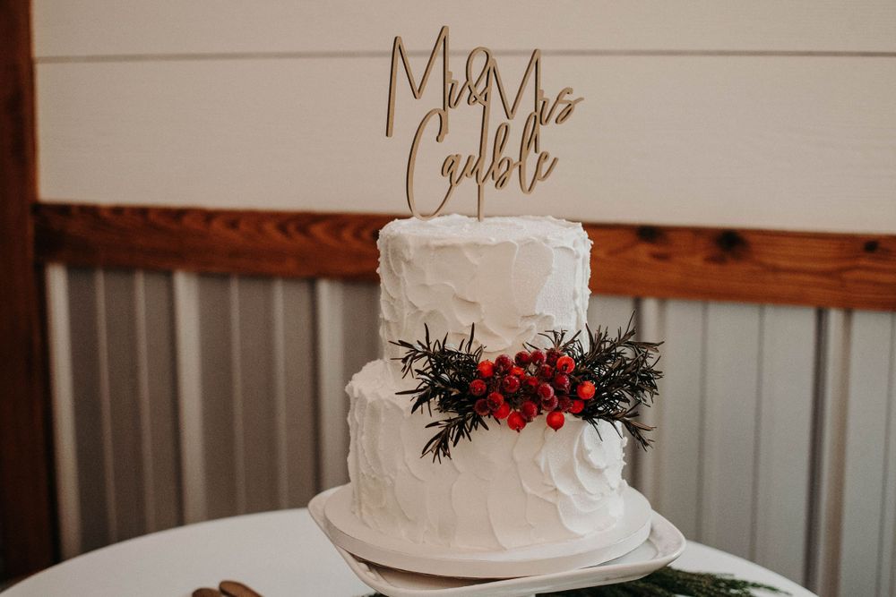 Two-tier white wedding cake with festive red berries and evergreen decoration.