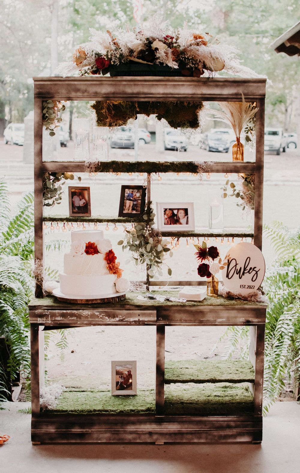 Rustic wooden display shelf decorated with floral arrangements and vintage photos for wedding reception.