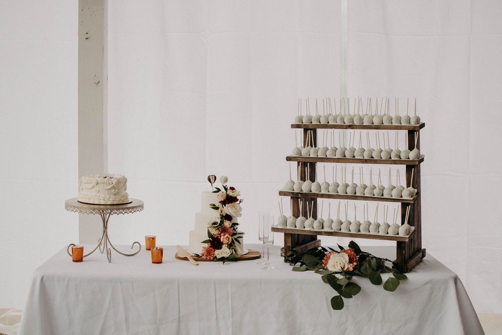 Minimalist wedding dessert table with tiered wooden stand and white cake on elegant tablecloth.