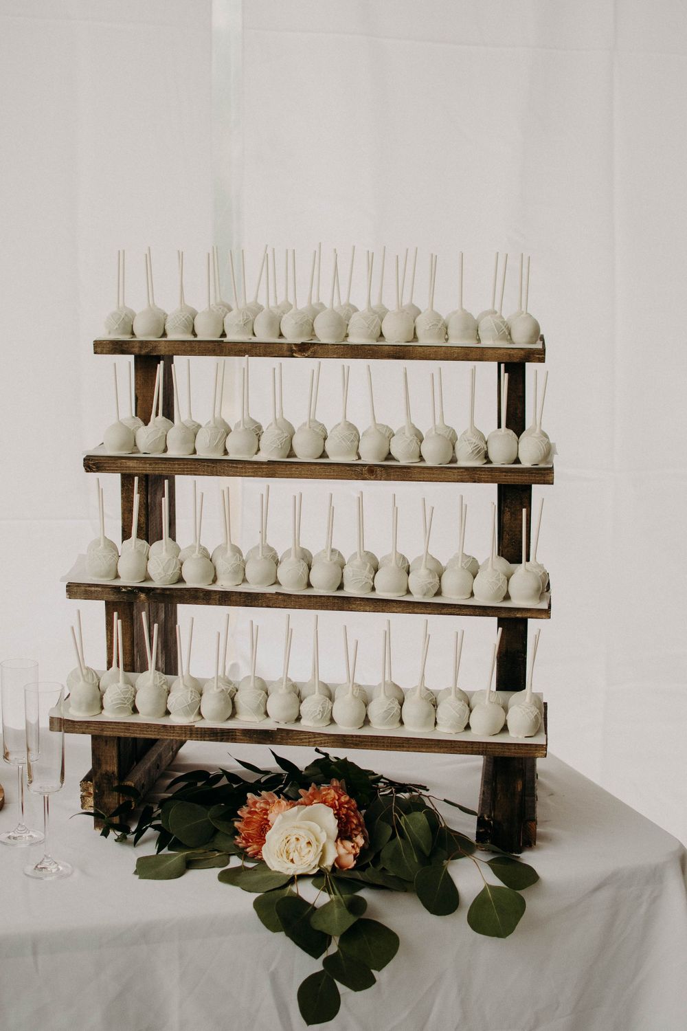 Four-tiered wooden display stand holding rows of white cake pops decorated with flowers.