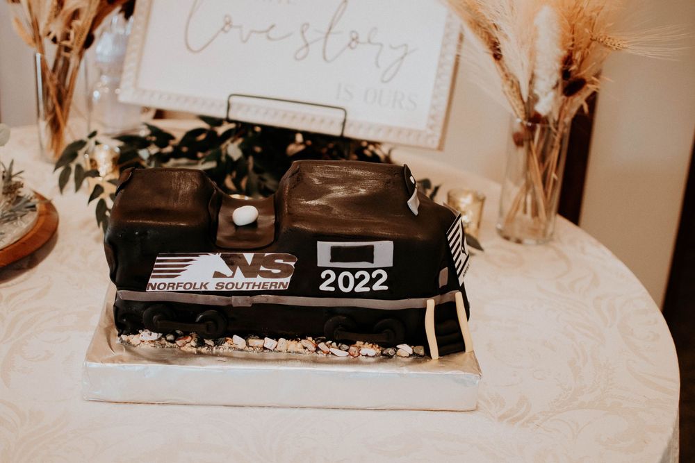 Unique black wedding cake decorated with 2022 displayed on a white tablecloth with dried pampas grass accents.