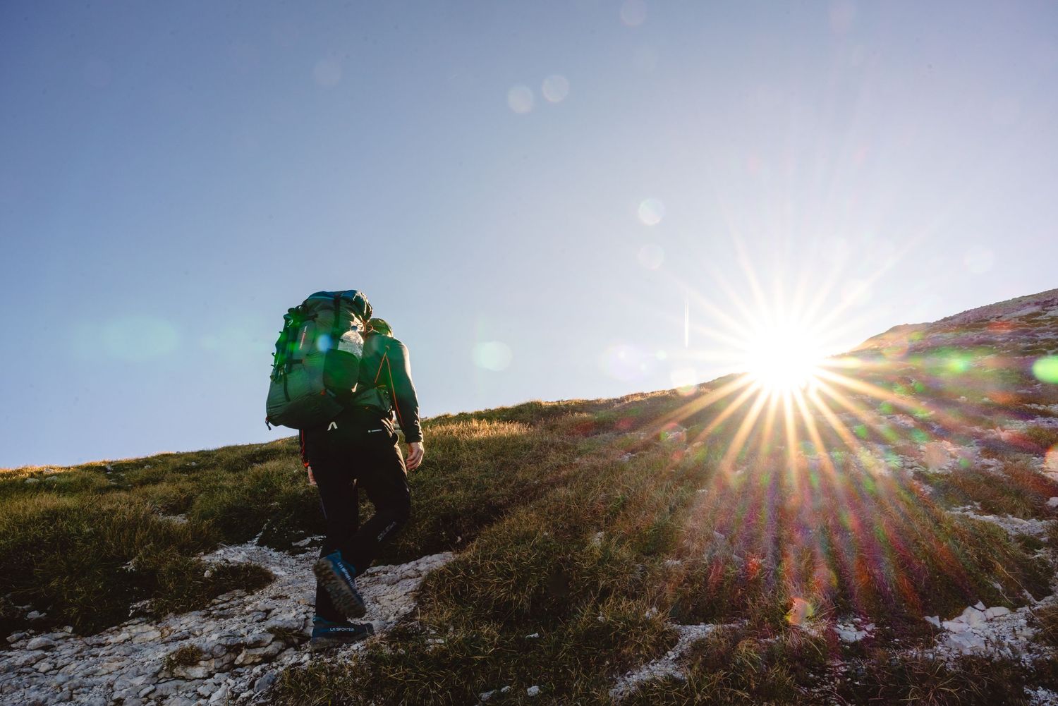 Hiker with backpack walking toward sunset on snowy mountain trail.