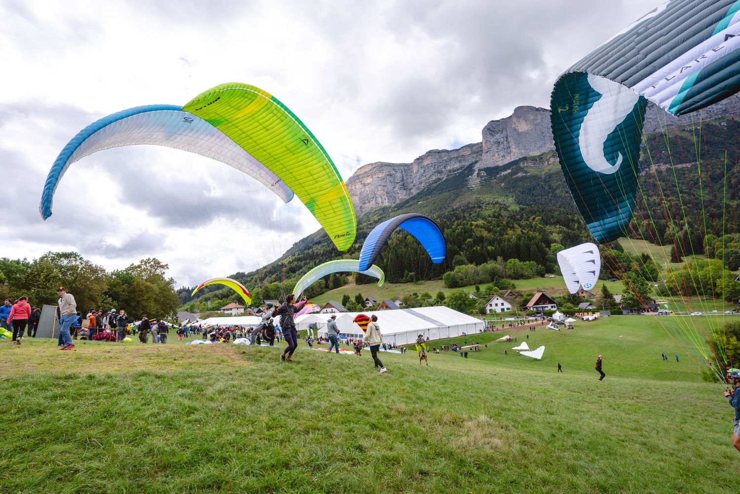Colorful paragliders preparing for takeoff in a green mountain valley.