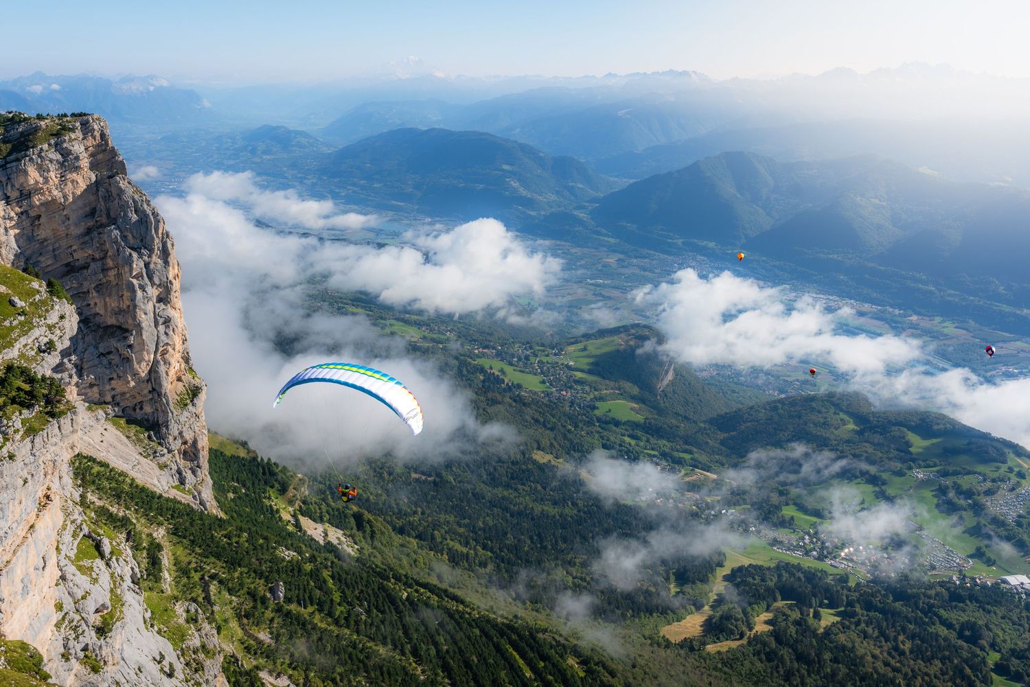 Paraglider soaring above misty mountain landscape with dramatic valley views.