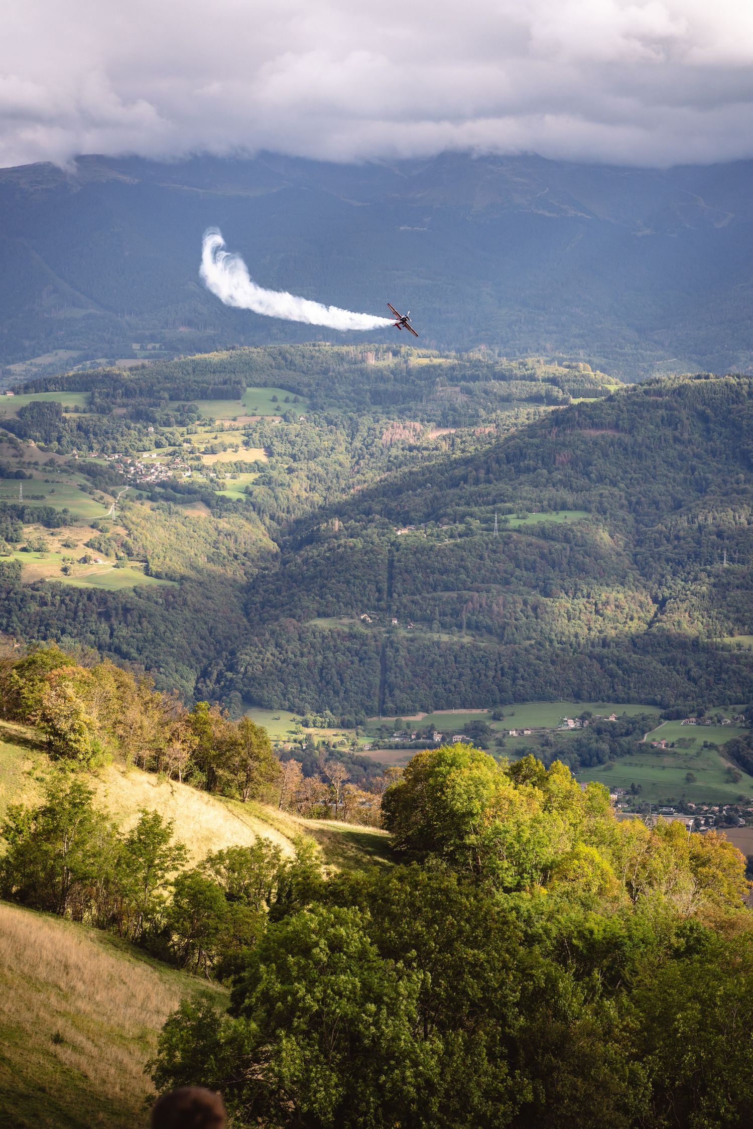 White paraglider wing soaring over green mountain valley landscape.