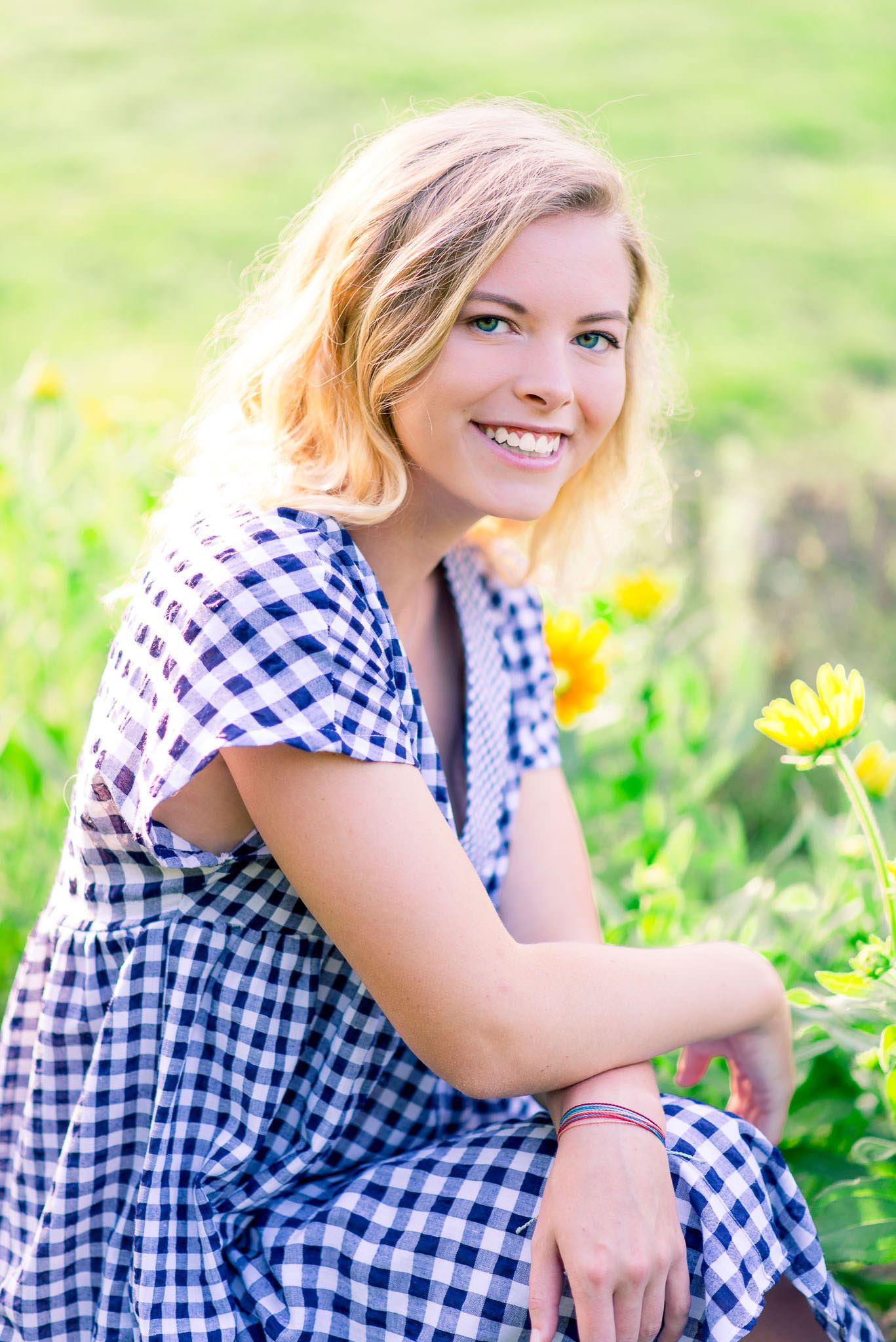 young blonde woman with blue eyes smiling and crouching in front of flowers in the summer