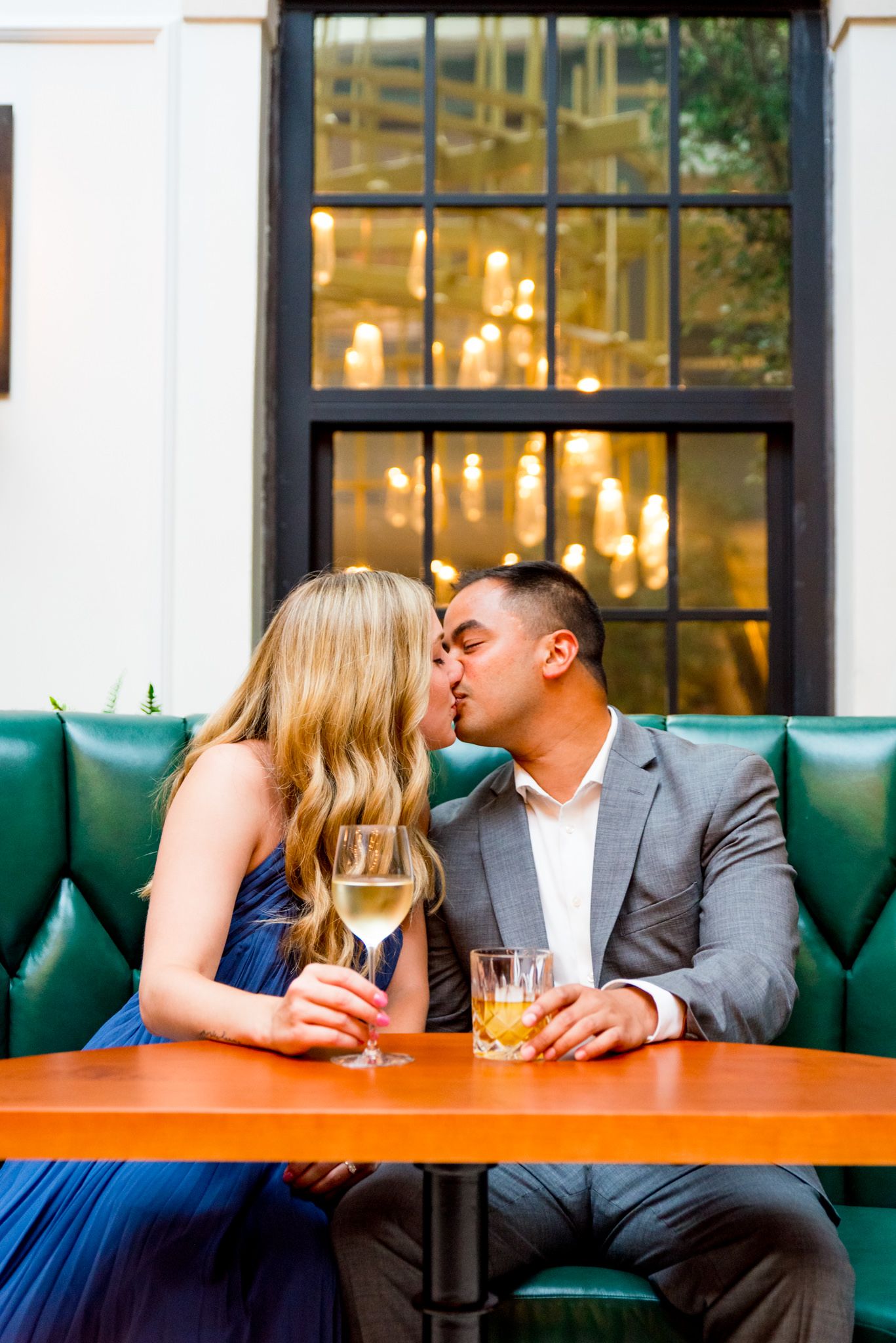 Asian man and blonde woman kiss in green booth at Lytle Park Hotel engagement session