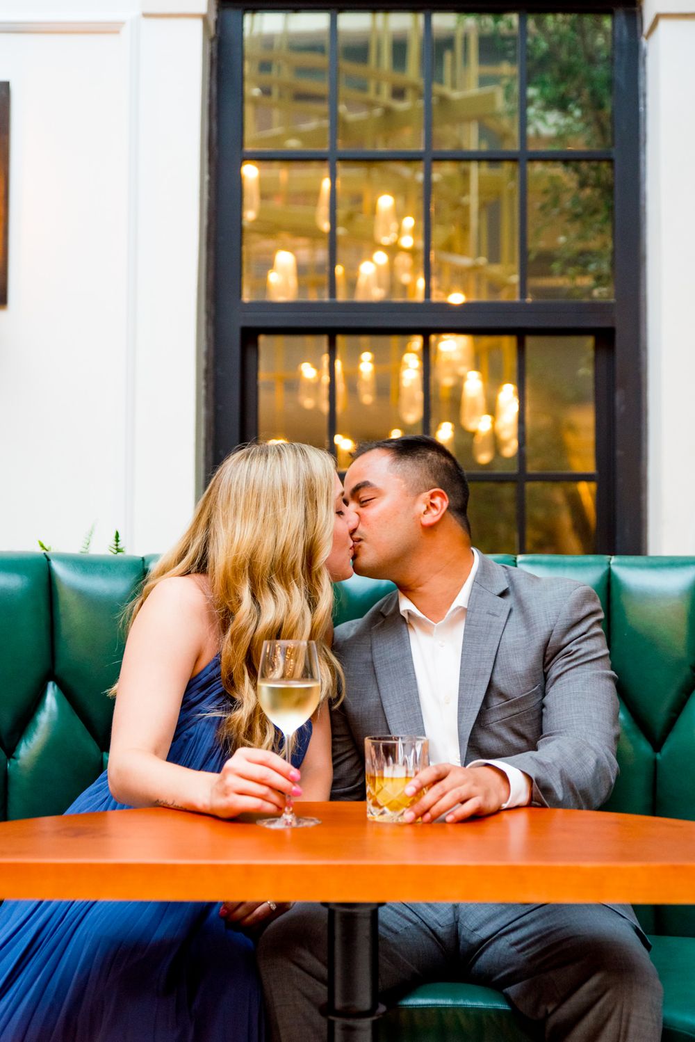 Asian man and blonde woman kiss in green booth at Lytle Park Hotel engagement session