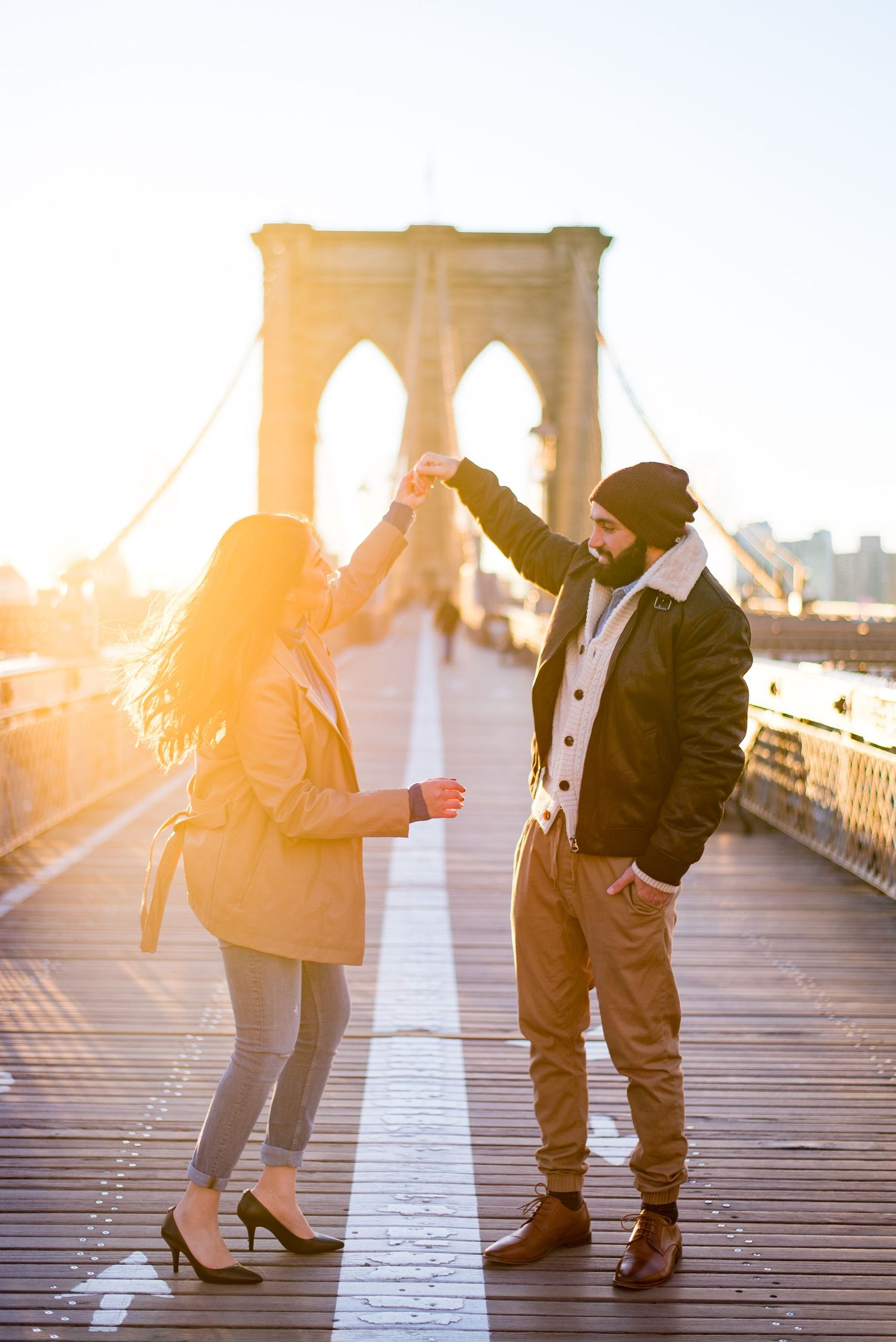 engaged man and woman twirling around in the middle of the Brooklyn Bridge in the morning at sunrise