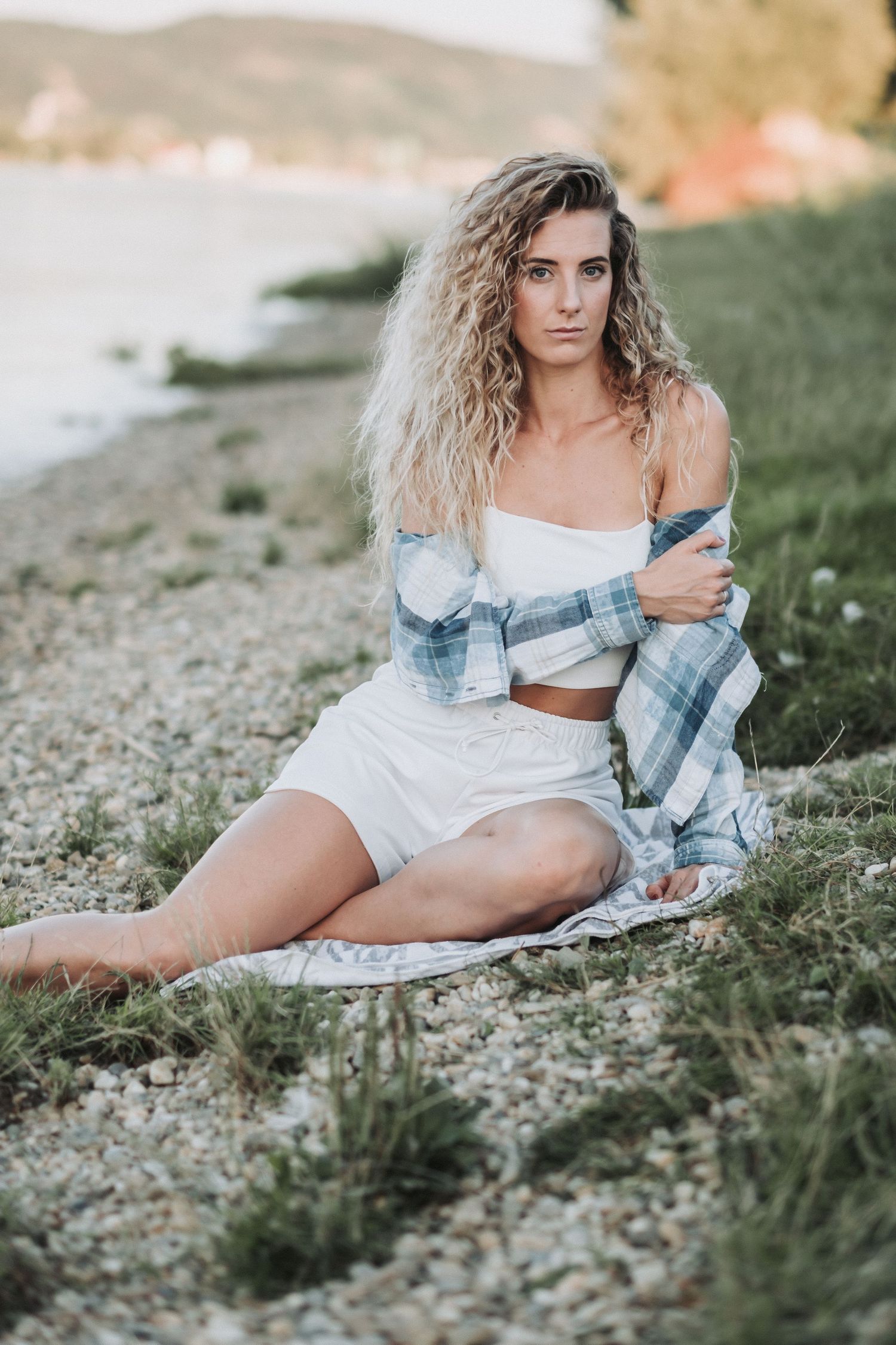 Lifestyle portrait on rocky beach wearing plaid overshirt and white summer outfit.