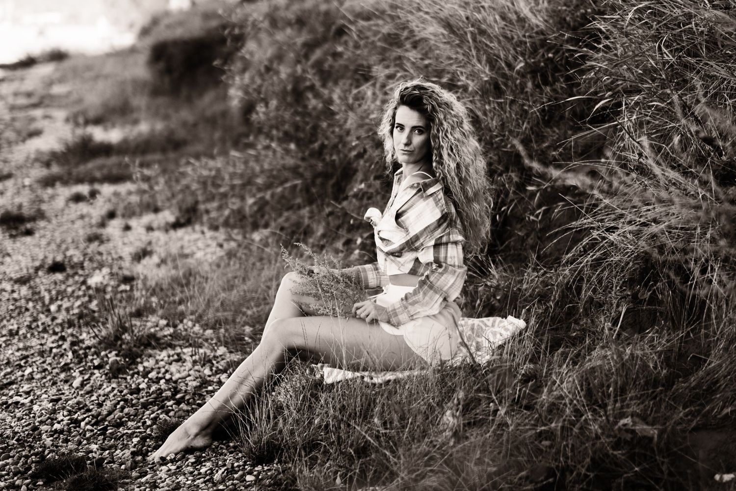 Monochrome fashion portrait on rocky beach with vintage styling.