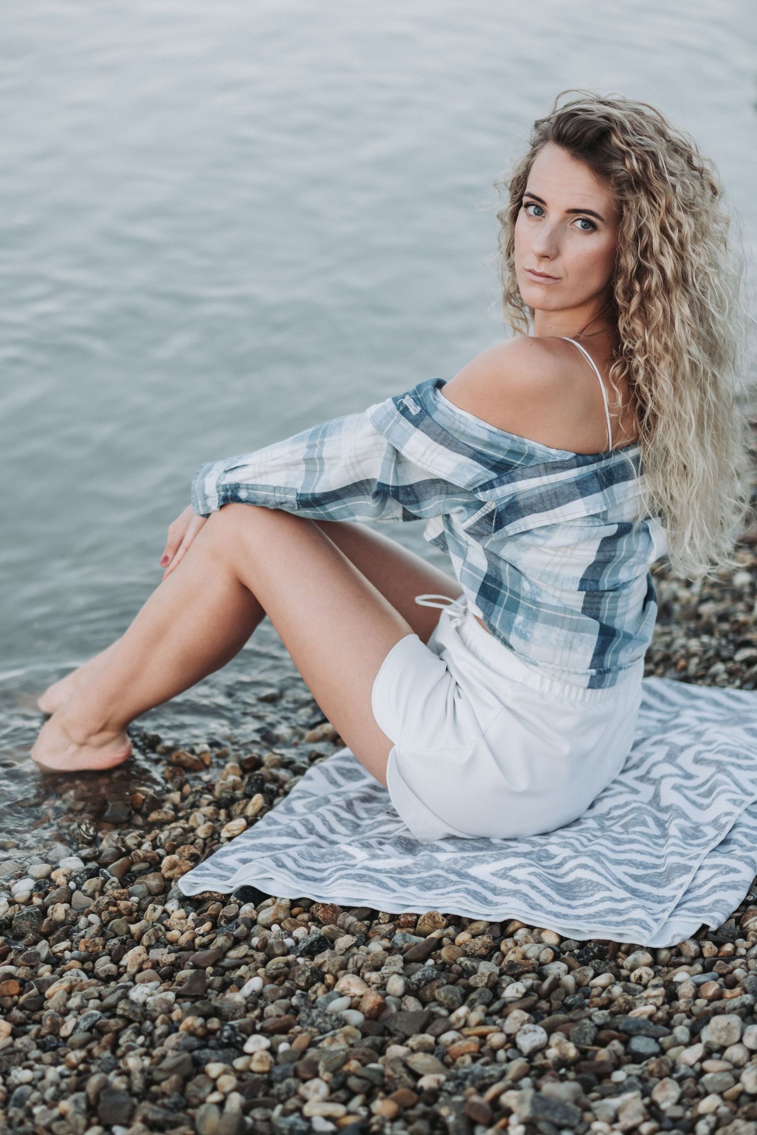 Seaside portrait on rocky beach wearing plaid shirt and white shorts.