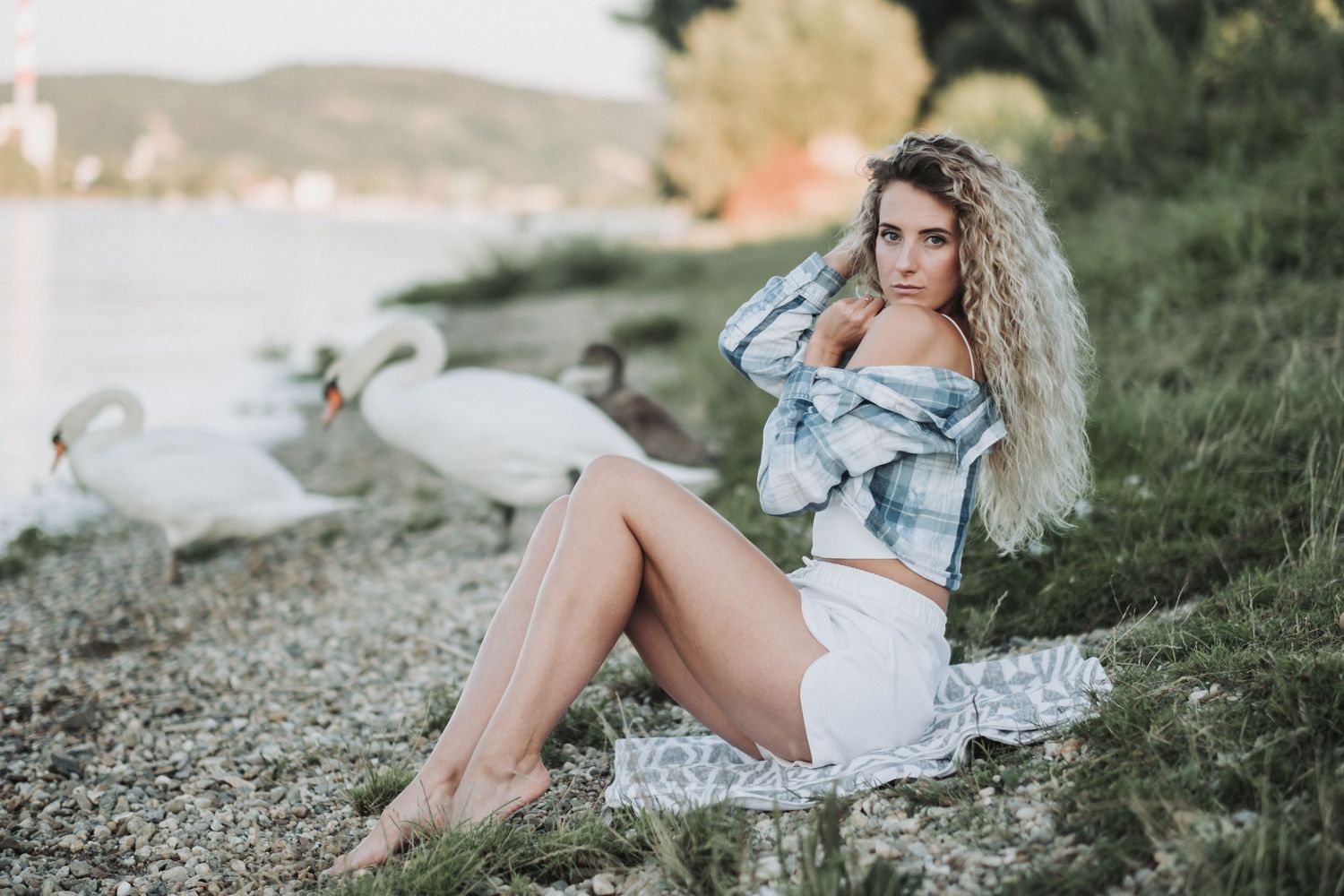 Casual summer portrait of woman in plaid top sitting on patterned blanket by water.