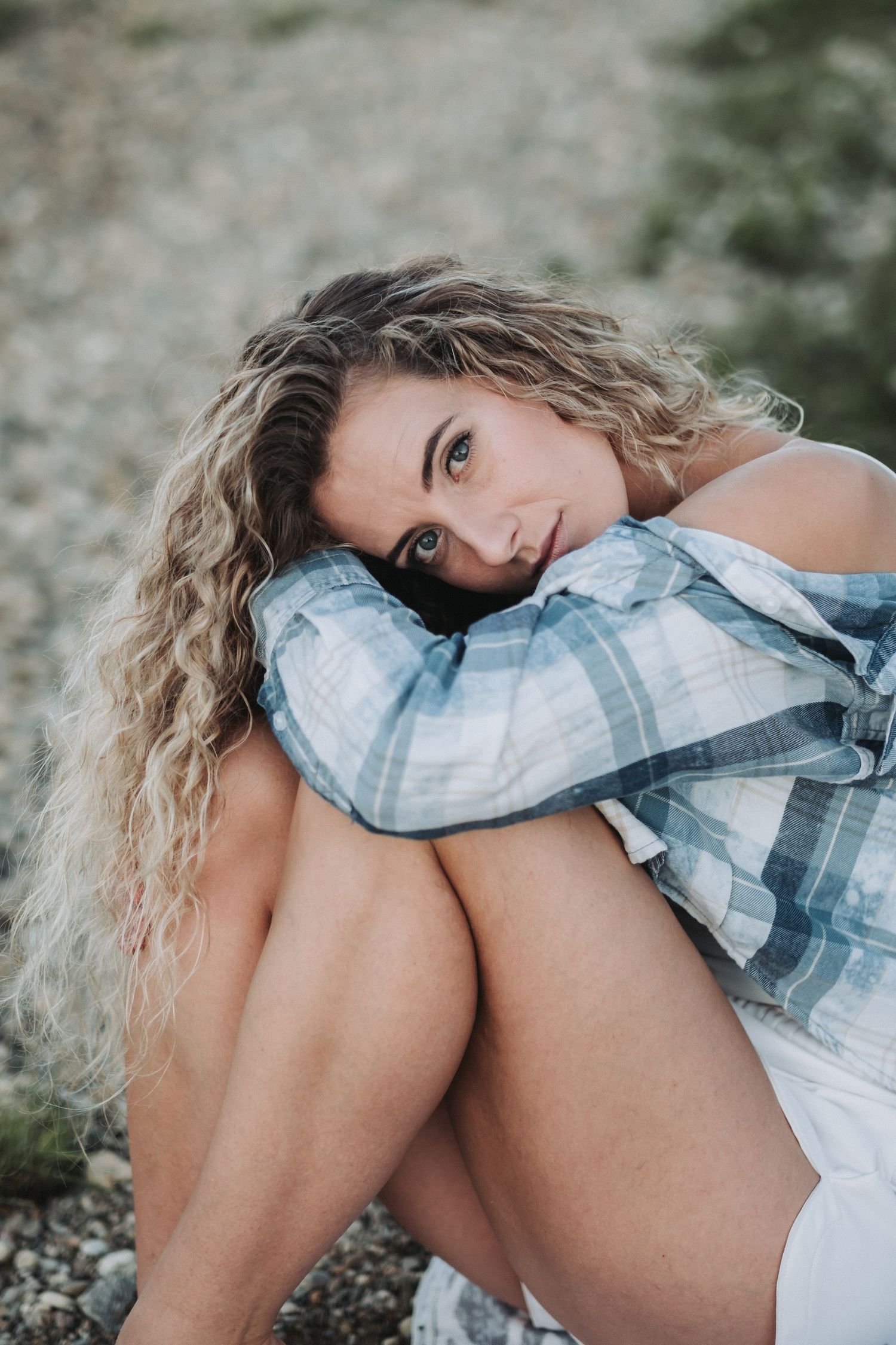 Moody close-up portrait on rocky beach with plaid shirt and natural styling.