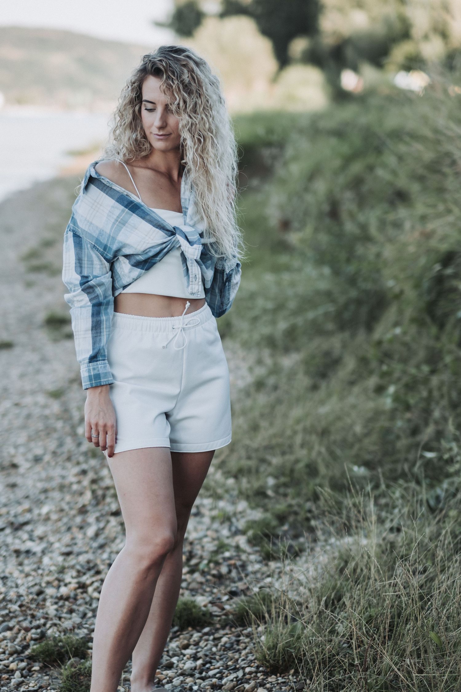Stylish beach fashion with plaid crop top and white shorts against coastal backdrop.