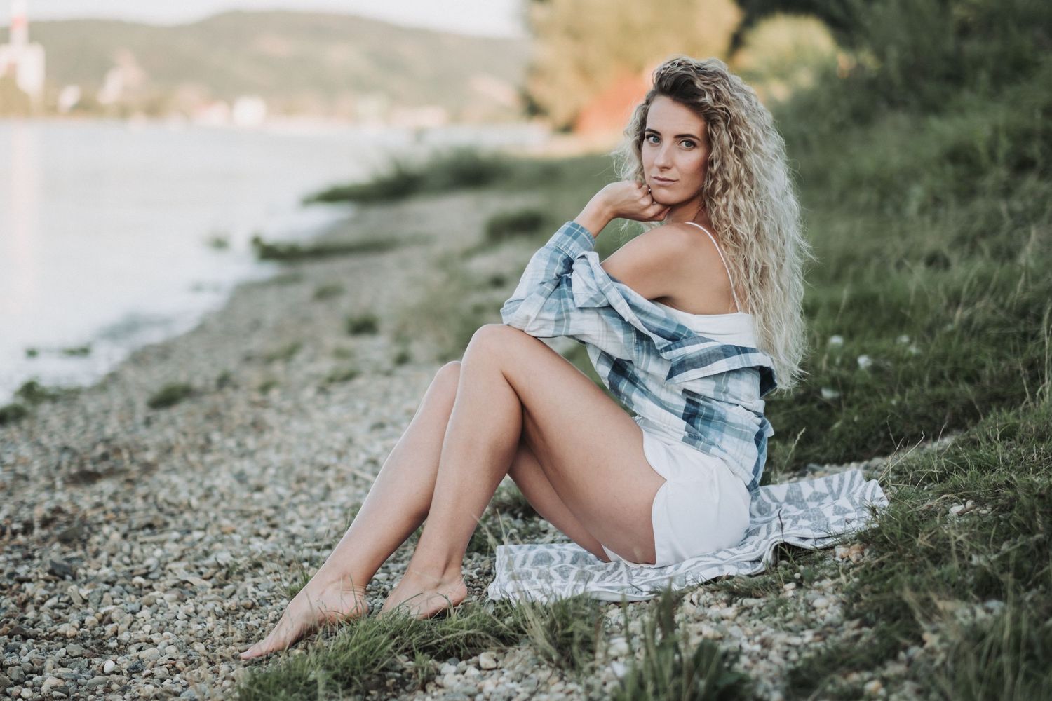 Beachwear fashion portrait with plaid top and white shorts against coastal scenery.
