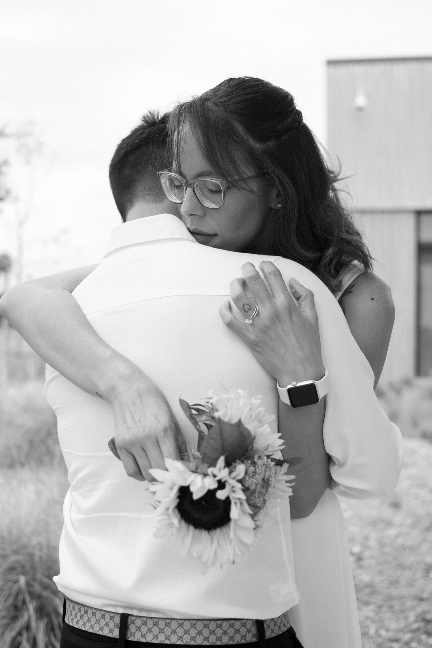 Black and white photo of embrace with sunflower bouquet.