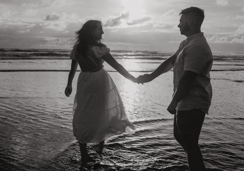 Couple dancing in ocean waves at sunset creating romantic silhouettes on the beach.